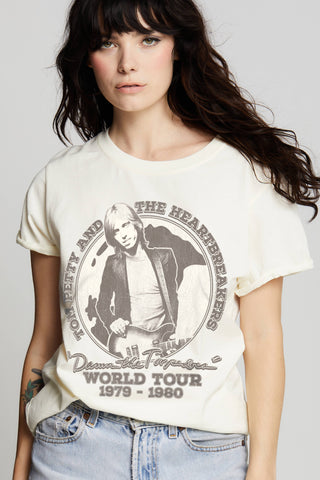 A woman with long dark hair is wearing a vintage-inspired Last Night Tom Petty World Tour tee from Recycled Karma, featuring a print of The Heartbreakers from their "Damn the Torpedoes World Tour 1979-1980." She is also wearing light blue jeans and standing in front of a plain background, making it perfect for any music lover.