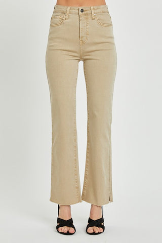 A person is wearing Tanda Curvy High-Rise Tummy Control Straight Pants by Risen. The beige pants offer a slim fit with a slight flare at the bottom, featuring a frayed hem and front pockets. Designed with subtle tummy control for added comfort, they are paired with black open-toe heels. The background is plain white.