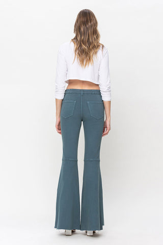 A person with long, wavy hair is standing with their back to the camera. They are wearing a white long-sleeved crop top and VERVET by Flying Monkey Delaney Super High Rise Wide Leg Jeans with frayed hems. The outfit is complemented by white platform shoes.