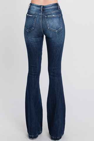The Chevelle Distressed Mid Rise Stretch Flare Jeans by Petra153 are showcased on someone from behind. These dark blue jeans feature two visible back pockets and white stitching along the seams, with slight fading on the back of the legs. With 5-pocket styling, they fit snugly around the hips and thighs before flaring out from the knees.