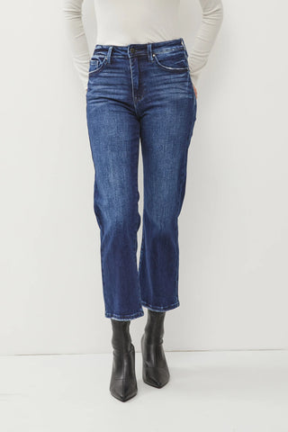 A person stands against a white background, wearing a white long-sleeve top, blue 0live High Rise Wide Leg Crop Jeans non distressed by Petra153 with slight fading on the thighs, and black ankle boots with pointed toes. The person's hands are placed in the front pockets of the jeans, creating a flattering fit for petite figures.