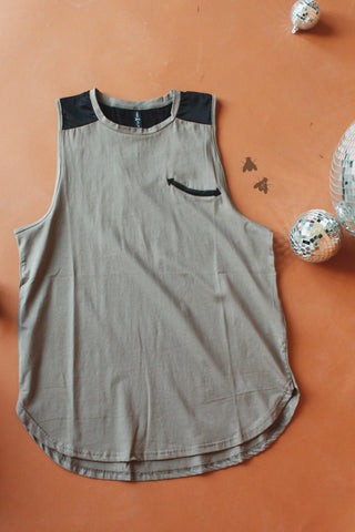 The Tanks to Wanette Tank by 2 Fly, a loose-fitting beige muscle tank with black shoulder accents and a small black chest pocket, is laid flat on an orange surface. Small silver disco balls and two bee illustrations surround the top.