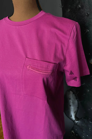 A mannequin displays the HANDY AS A POCKET* POP by Western Edge Boutique, a vibrant pink T-shirt featuring a stitched pocket on the left chest and small insect graphics on the sleeve. The excellent fabric contrasts beautifully with the dark, textured background.
