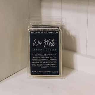 A pack of Wax Melts in your favorite laundry soap from Western Edge Boutique, infused with rich fragrances, rests on a white wooden surface. The modern black label features white text detailing usage instructions and company information.