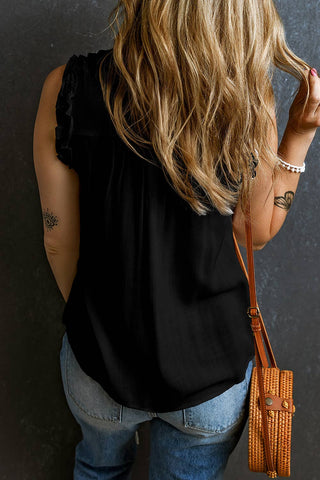 A woman with long, wavy blonde hair is facing away from the camera. She is wearing a black Hemslee Button Split Neck Frilly Detail Tank Top from Little Daisy Closet and blue jeans, perfect for spring and summer wear. Carrying a small woven crossbody bag, she reveals an eye tattoo on her right arm and a bracelet on her left wrist.