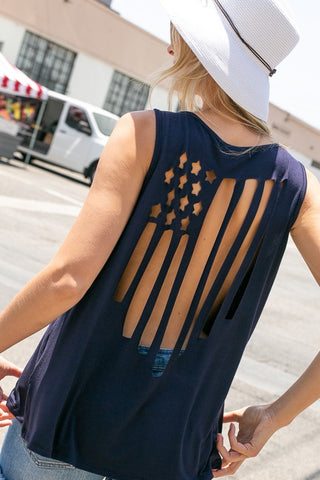 A person with long hair, wearing a white sunhat and a sleeveless "Spangled Tank Flag Cut Out Tank Top" by Western Edge Boutique, stands outdoors near a white van and other market stands, embracing USA pride during the July 4th celebrations.