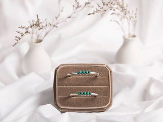 On a velvet jewelry holder, the Turquoise & Sterling Silver Cluster Cuff Bracelet from Moxie Maine is showcased. The bracelet, made with sterling silver and adorned with multiple small turquoise gemstones, is set against a backdrop of soft white fabric and flanked by two small white vases containing dried branches, which together create a minimalistic and delicate aesthetic.