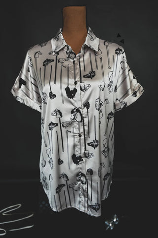 A white, short-sleeved, button-up shirt with a collar from the 2FLY brand's "All the Ponies" collection is displayed on a mannequin against a dark background. The shirt features black and grey abstract designs connected by thin vertical lines, giving it a retro fit vibe. The fabric has a slightly shiny, satin-like texture.