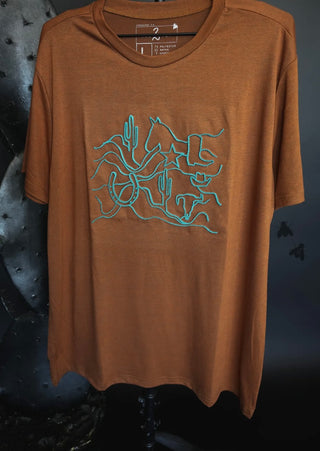 The Romee Ranch Road Graphic Tee by 2FLY hangs on a display in front of a dark, textured background. The brown shirt features a blue line drawing of a desert landscape that includes cacti, a horse, a boot, and other Western-themed elements.