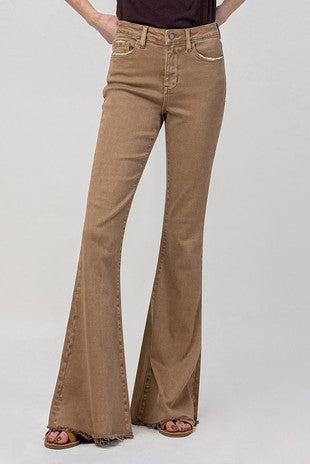 Person wearing the "Dusty Mocha Bells" by Western Edge Boutique, featuring high-rise, super flare design and paired with a dark top, with hands in their pockets. The jeans have a front button and zip closure, made from comfort stretch denim. They are also wearing brown sandals. The image is cropped above the shoulders.