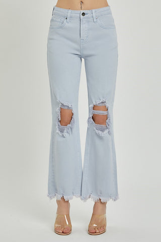 A person wearing light blue Brea Curvy High-Rise Straight Pants by Risen, featuring frayed hems and large distressed rips on both knees. They are also sporting clear high-heeled sandals. The photo is a front view, cropped just above the torso.