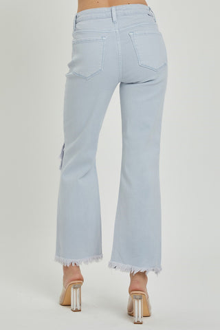 A person wearing Brea High-Rise Straight Pants from Risen in light blue is shown from the back. They are standing with their feet apart, sporting clear, chunky-heeled shoes. The pants feature back pockets, a seam detail down the sides, and distressed knees for a trendy touch.