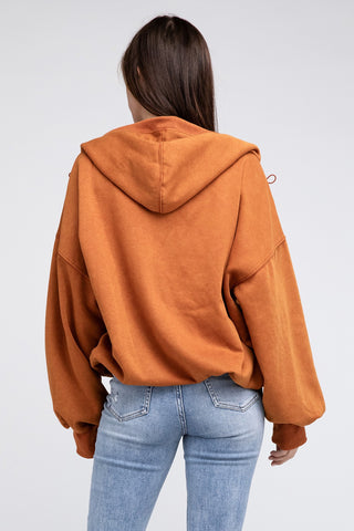 A person with long hair is showcasing their fashion style by wearing the Burke Quarter Zip Stitch Detailed Elastic Hem Hoodie from Western Edge Boutique, paired with blue jeans, facing away from the camera. The hood is down, allowing the outfit to stand out against the plain, light-colored background.