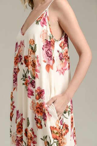 The individual is wearing the VANILIA BAY Ava Floral Summer Dress Curvy, a sleeveless, loose-fitting dress adorned with a mix of pink, orange, and green flowers on a light background. With their left hand resting in a pocket of this lightweight tank dress, it radiates effortless summer charm.