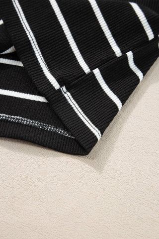 Close-up of a folded Kannon Stripe Ribbed Knit Tank Mini Dress in black from Little Daisy Closet, featuring bold horizontal white stripes. The focus is on the texture of the fabric and the intricate stitching along the edge. This casual summer dress rests on a light beige surface, showcasing its relaxed yet stylish appeal.