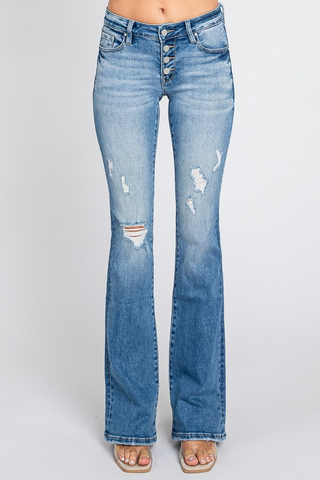A person wearing Petra153's Chance Button Up Low Rise Destroyed Jeans with distressed details on the thighs and knee. The jeans feature an exposed button fly closure and have a slight fade. The person is barefoot, standing against a plain white background.