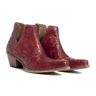 The Moxie Hand-tooled Booties in Scarlet by Myra are crafted from red leather with intricate floral embossing and feature a hand-tooled pattern. These Western booties have a side cut-out design, a low wooden heel, and a polished finish. They are displayed against a white background.