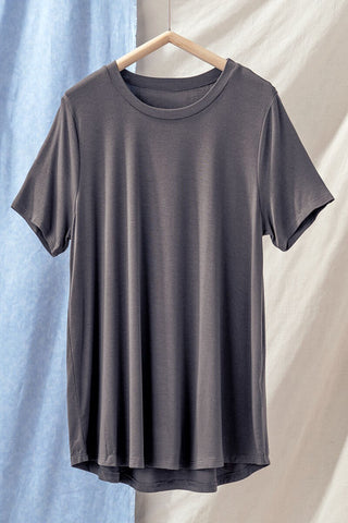 The luxuriously soft Cassidy Soft Casual Crew Neck Tee by Trend Notes, crafted from a bamboo and viscose blend, hangs on a wooden hanger against a backdrop of light blue and beige fabric.