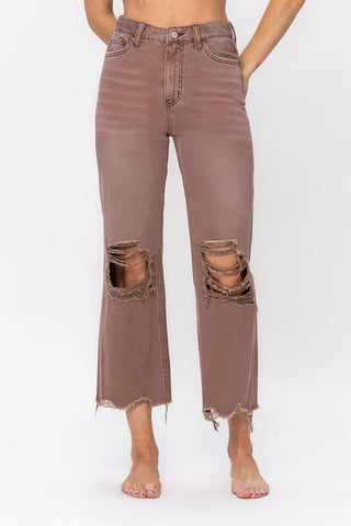 A person wearing VERVET by Flying Monkey's Beckit Saddle Distressed Vintage Crop Flare Jeans stands barefoot against a plain white background. The high-waisted, flare jeans feature ripped knees, frayed hems, front and back pockets, along with a visible button closure and zipper fly.