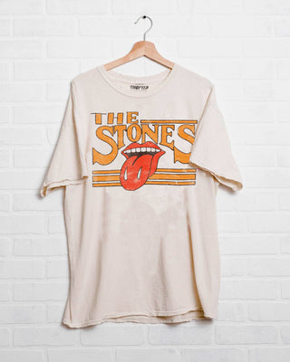 A Jolie Rolling Stones Stoned Off White Thrifted Tee from Western Edge Boutique hanging on a wooden hanger against a white brick wall. The officially licensed shirt features a vintage design with "The Stones" written in bold letters and the iconic red tongue and lips logo below the text.