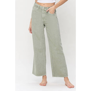 A person is modeling the Kimsie Super High Ankle Wide Leg Jeans by VERVET by Flying Monkey. The non-stretch sage green denim offers a structured look as the person, barefoot and with hands resting in the front pockets, showcases the stylish cut from waist to slightly below the ankles against a plain white background.