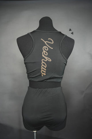 A black mannequin is dressed in a sleek black sleeveless crop top paired with matching high-waisted CABO COWBOY BOTTOMS from 2 Fly. The crop top features the word "Yeehaw" embroidered in a rope-like design on the back, and the backdrop is a neutral gray.