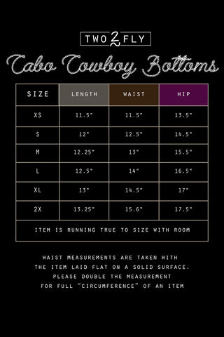 The 2 Fly "CABO COWBOY BOTTOMS" size chart includes sizes XS to 2X, detailing measurements for length, waist, and hip. Note that measurements are given as halves; double them for full circumference. These black swim bottoms with silver studs fit true to size with a bit of extra room.