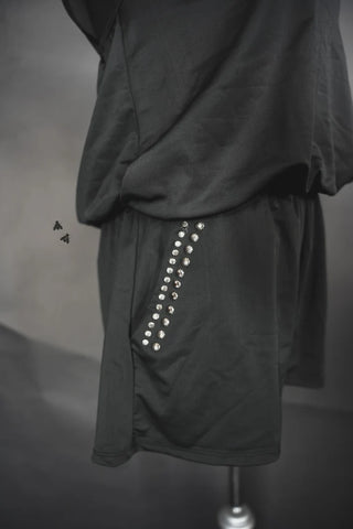 Close-up of the Rowdy Mama Swim Romper, a dark outfit by 2 Fly adorned with small, shiny studs arranged in a row on the side. The upper part appears to be draped fabric, creating soft folds offering modest coverage. The outfit is displayed on a mannequin, and two small black flies are visible in the frame.