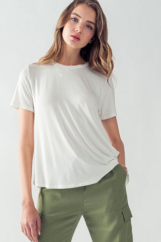 A young woman with long wavy hair is wearing a casual outfit consisting of the Cassidy Soft Casual Crew Neck Tee by Trend Notes paired with olive green cargo pants featuring pockets. Crafted from a blend of bamboo and viscose, the luxuriously soft tee accentuates her relaxed expression as she stands against a plain white background, gazing directly at the camera.